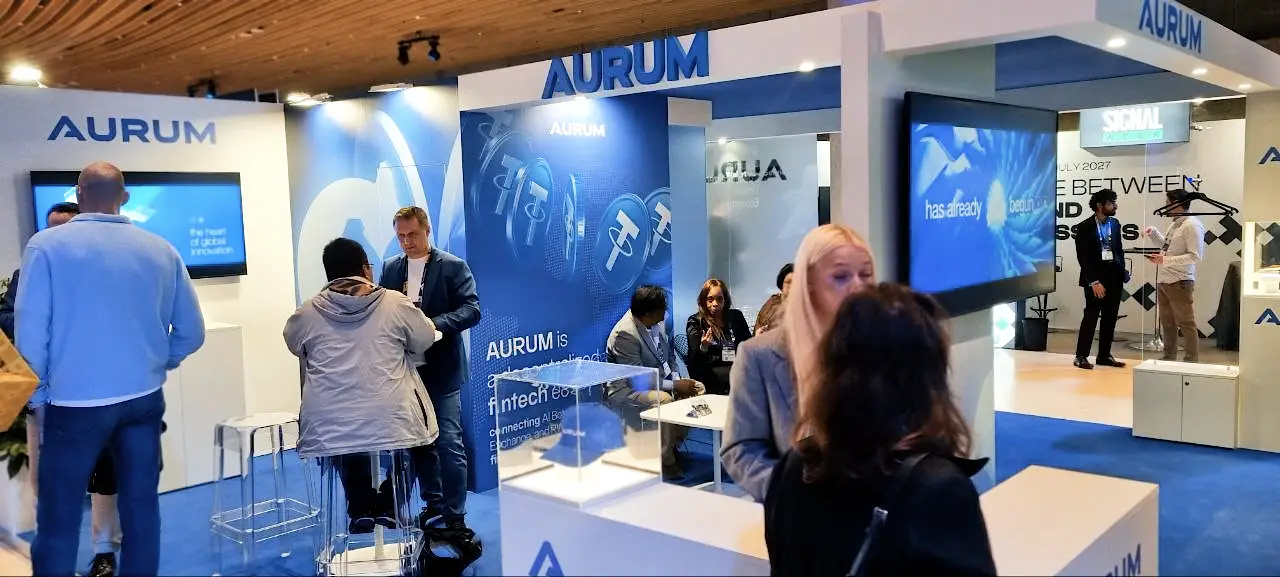 Aurum company booth at Paris Blockchain Week featuring fintech ecosystem branding and digital displays.