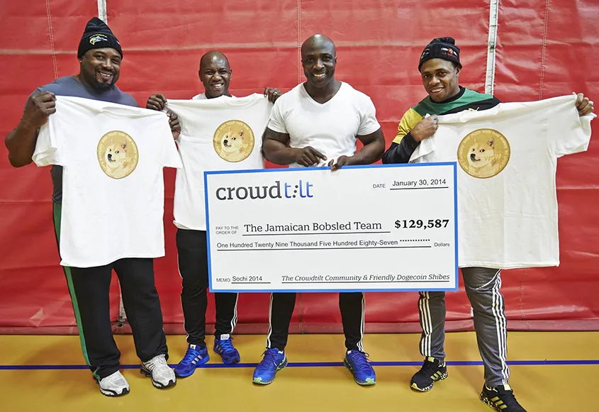 Four men standing, holding a large donation check "$129,587" dated "January 30, 2014." Tree of the men are holding up white T-shirts featuring the Dogecoin logo.