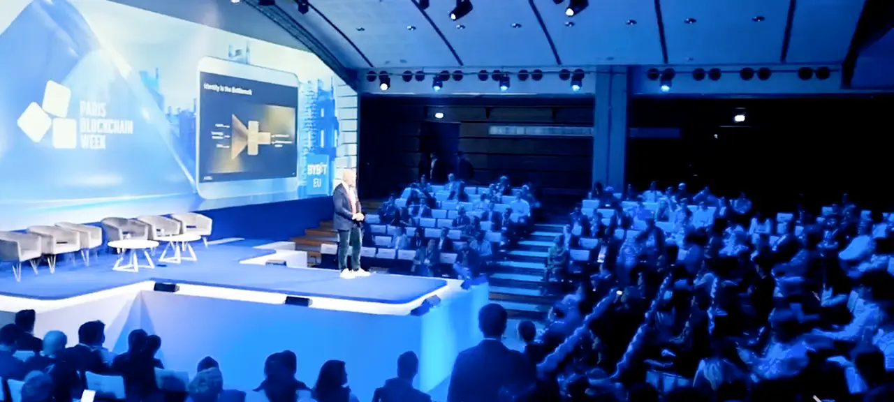 Frederik Gregaard from the Cardano Foundation speaking on the main stage at Paris Blockchain Week 2026, with a presentation slide on identity displayed behind him.