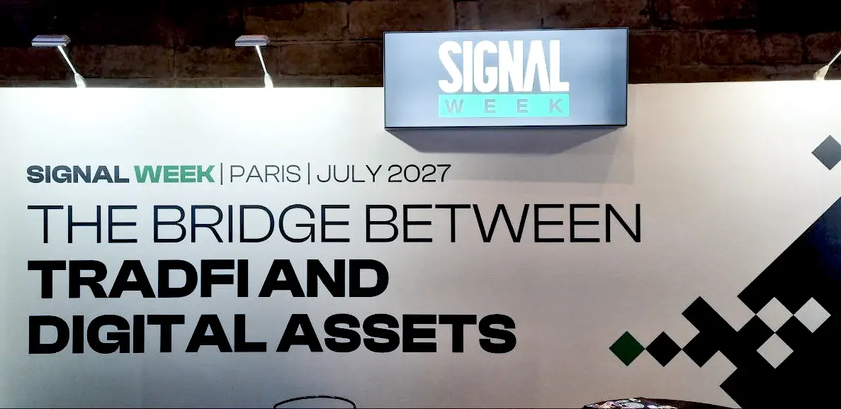 Large white sign at Paris Blockchain Week promoting Signal Week Paris in July 2027, with the text "THE BRIDGE BETWEEN TRADFI AND DIGITAL ASSETS."